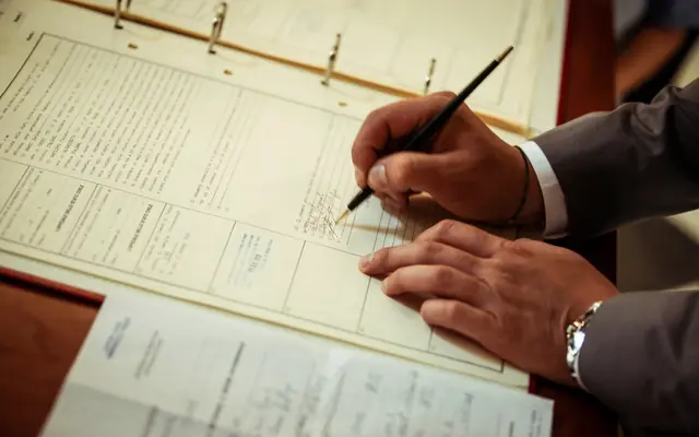 Persona firmando documentos en una carpeta con expedientes