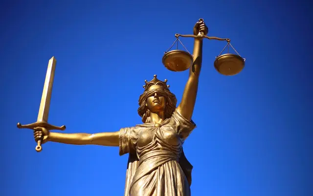 Estatua de la justicia con espada y balanza bajo un cielo azul