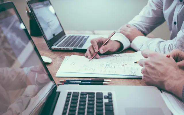 Personas revisando documentos junto a un notebook